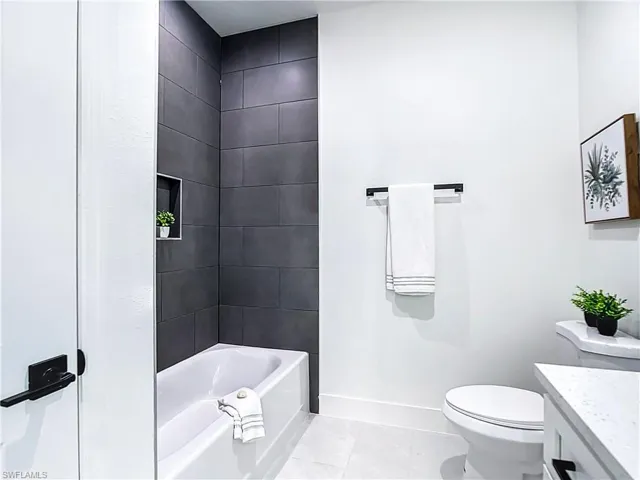 White bathtub with dark gray subway tile surround and integrated shower niche