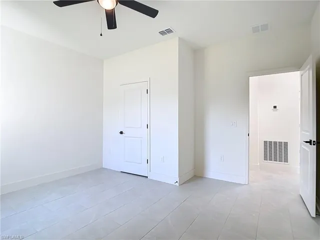 Spacious room featuring light-toned tile flooring, clean white walls, and a ceiling fan with integrated lighting