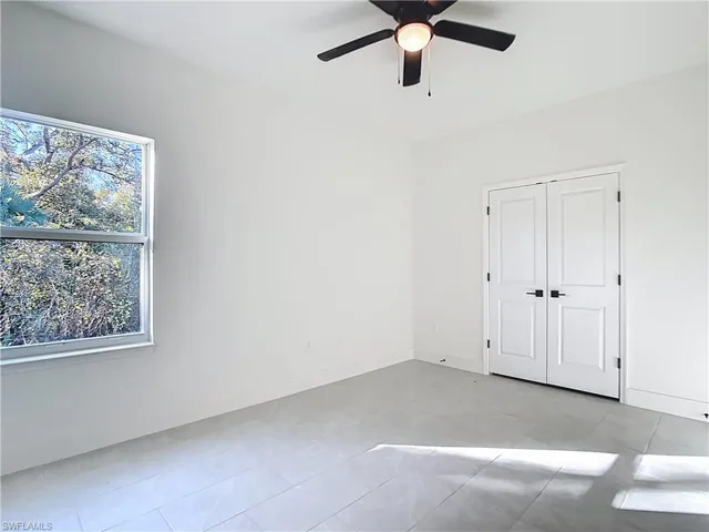 Spacious room featuring light gray tile flooring, a contemporary ceiling fan with integrated lighting, and a double-door closet with matte black hardware