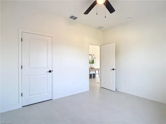 Spacious room featuring light-colored tile flooring, white walls, and a ceiling fan with black blades