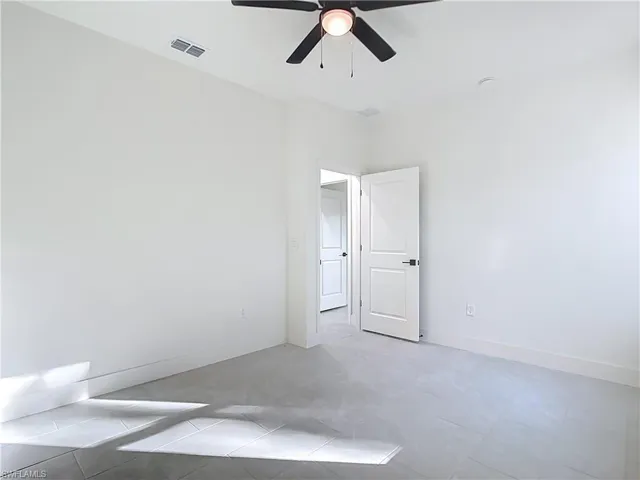 Spacious interior room featuring light gray tile flooring, crisp white walls, a modern ceiling fan with integrated lighting, and white interior doors with black hardware