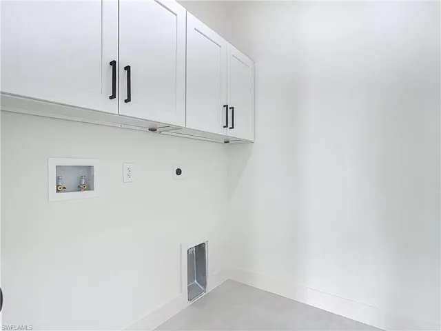 Utility room featuring overhead white cabinetry with black hardware, washer/dryer hookups, and light-toned flooring