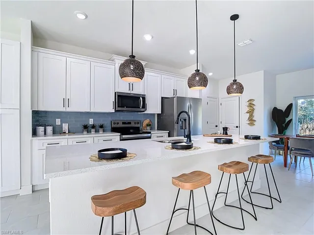 Modern kitchen featuring a large central island with seating, white shaker cabinetry, stainless steel appliances, and a blue subway tile backsplash