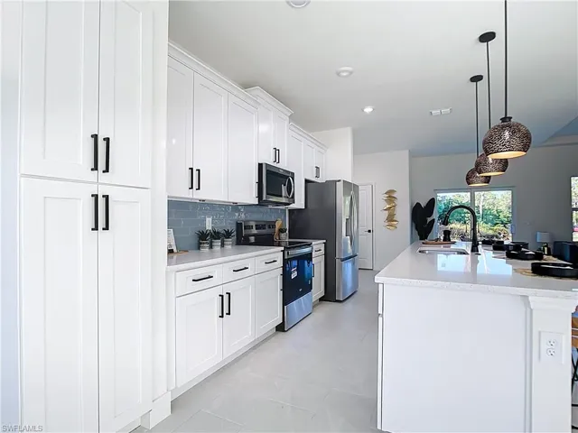 Kitchen featuring white shaker cabinetry, stainless steel appliances, light-toned countertops, and a subway tile backsplash