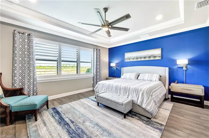 Bedroom with baseboards, visible vents, a raised ceiling, wood finished floors, and crown molding