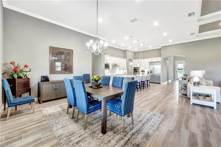 Dining area with visible vents, arched walkways, wood tiled floor, crown molding, and a notable chandelier