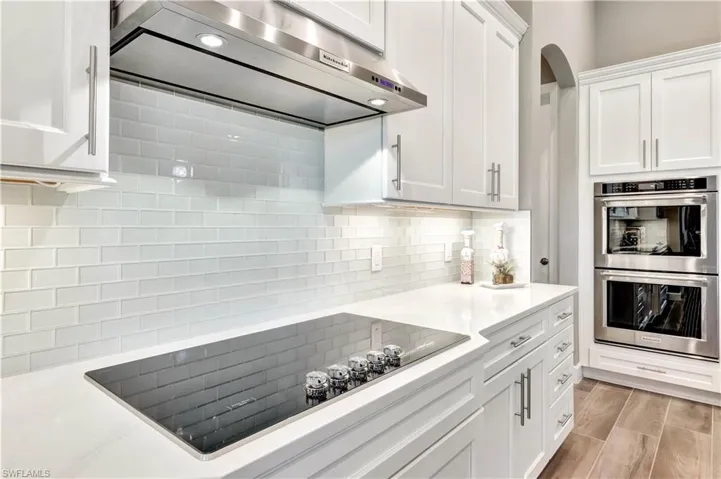 Kitchen featuring black electric stovetop, stainless steel double oven, white cabinetry, light countertops, and range hood