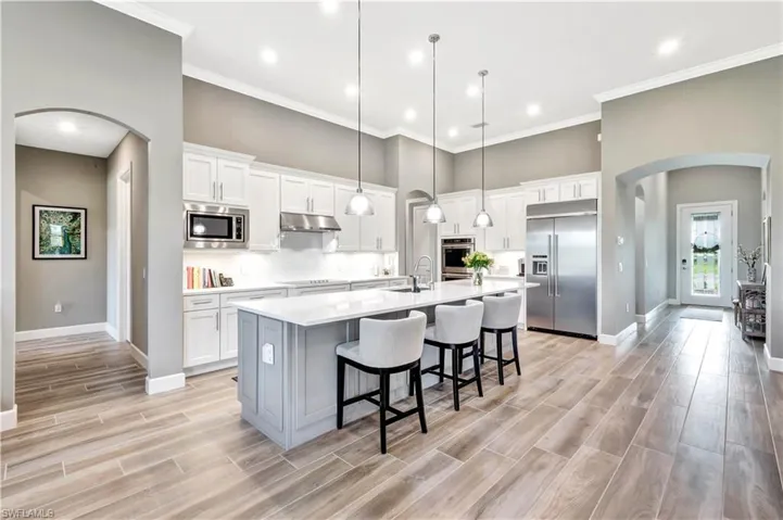 Kitchen featuring a kitchen island with sink, arched walkways, light countertops, and built in appliances