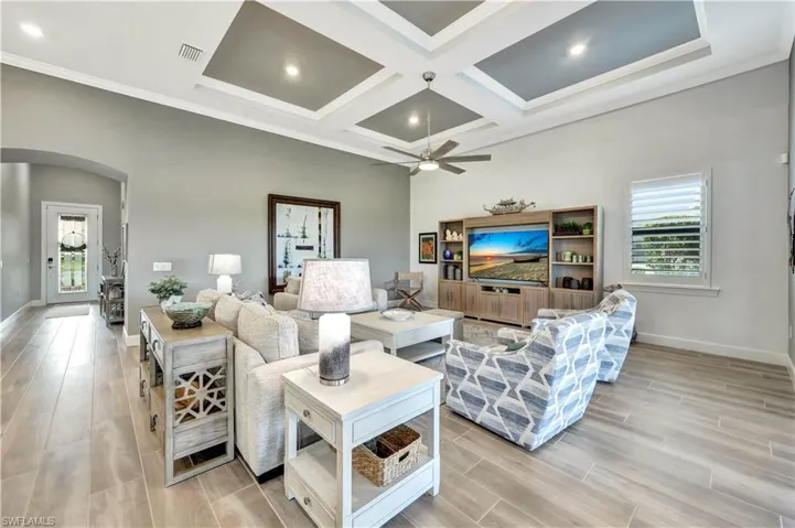 Living area featuring arched walkways, coffered ceiling, baseboards, and wood tiled floor