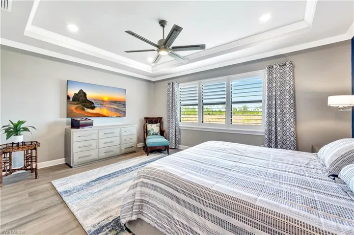Bedroom with ornamental molding, a tray ceiling, light wood-style floors, and baseboards