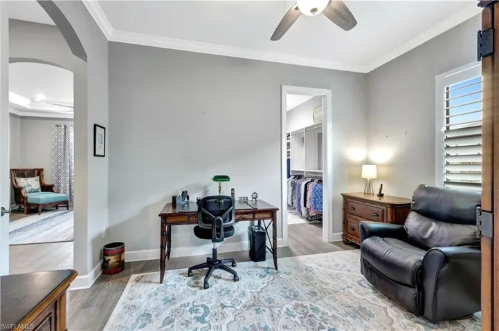 Office space with arched walkways, light wood-style flooring, a ceiling fan, baseboards, and crown molding