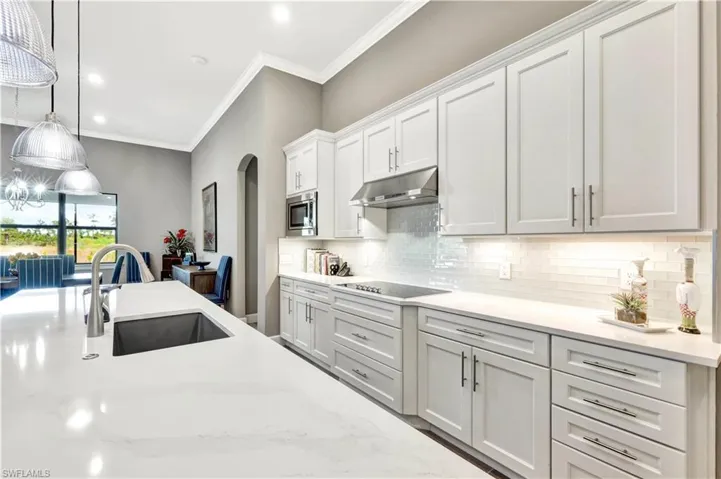 Kitchen with arched walkways, decorative light fixtures, under cabinet range hood, white cabinetry, and a sink