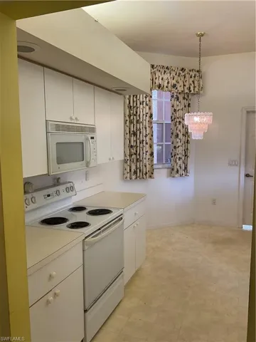 Kitchen featuring white cabinets, a notable chandelier, light countertops, decorative light fixtures, and range