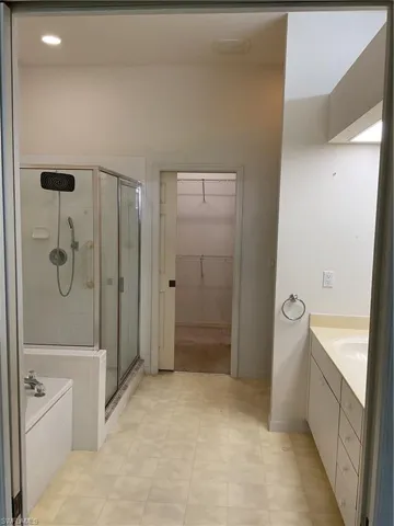 Bathroom featuring a walk in closet, a shower stall, a garden tub, and vanity