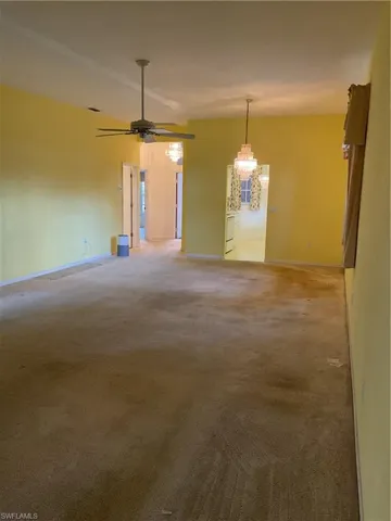 Unfurnished room featuring ceiling fan with notable chandelier, light carpet, and baseboards