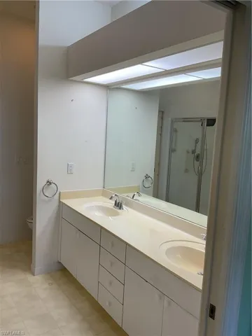 Full bathroom featuring toilet, a sink, double vanity, and a stall shower
