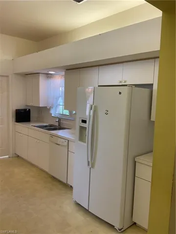 Kitchen with a sink, white cabinetry, dishwashing machine, light countertops, and refrigerator with ice dispenser