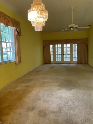 Spare room with visible vents, french doors, baseboards, carpet flooring, and ceiling fan with notable chandelier