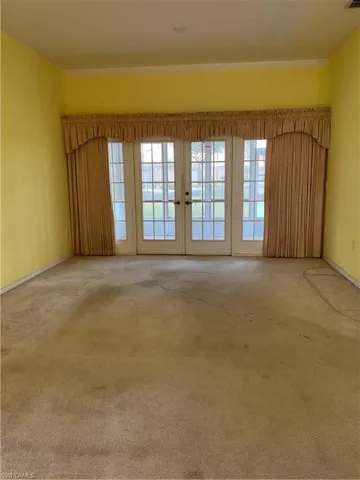 Carpeted spare room with baseboards and french doors
