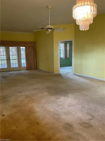 Carpeted spare room featuring baseboards, french doors, and ceiling fan with notable chandelier