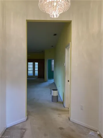 Corridor featuring baseboards, visible vents, carpet floors, and a notable chandelier