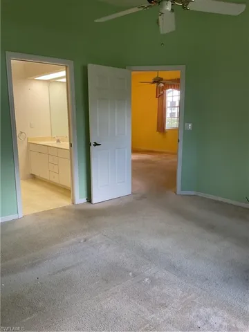 Unfurnished bedroom with light colored carpet, baseboards, a ceiling fan, and ensuite bathroom