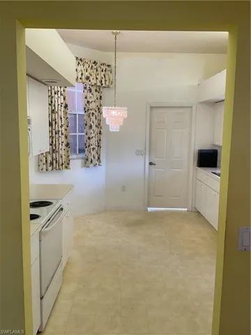 Kitchen featuring hanging light fixtures, range, light countertops, white cabinets, and a notable chandelier