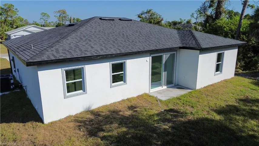 Back of house featuring a yard, stucco siding, roof with shingles, and a patio area