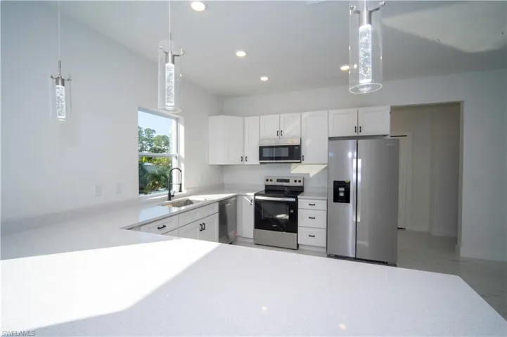 Kitchen featuring appliances with stainless steel finishes, white cabinetry, decorative light fixtures, recessed lighting, and light stone counters