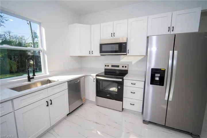 Kitchen with stainless steel appliances, white cabinets, light marble finish flooring, and light stone counters