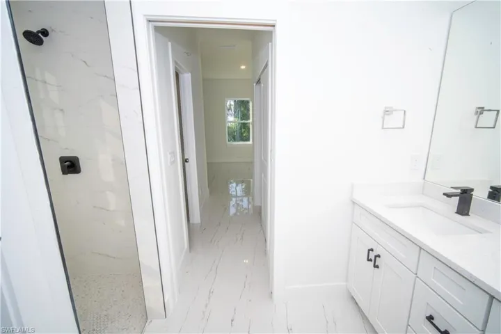 Full bath with light marble finish flooring, a marble finish shower, and vanity
