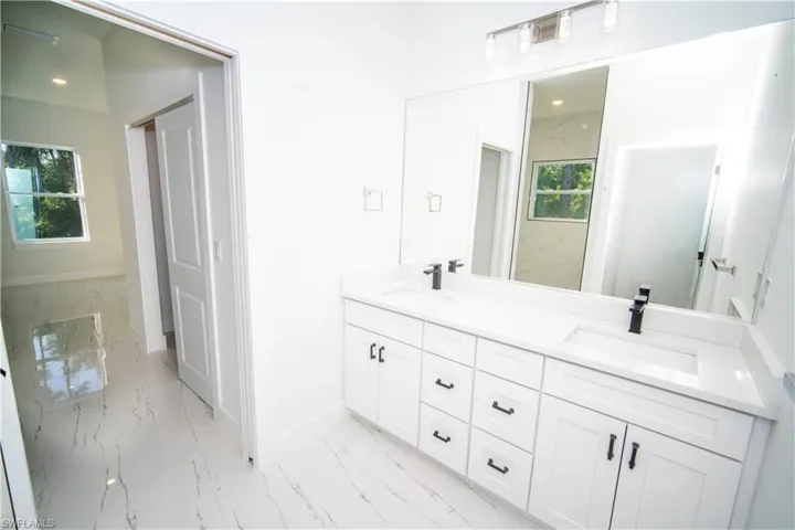 Full bathroom featuring double vanity, light marble finish floors, and plenty of natural light