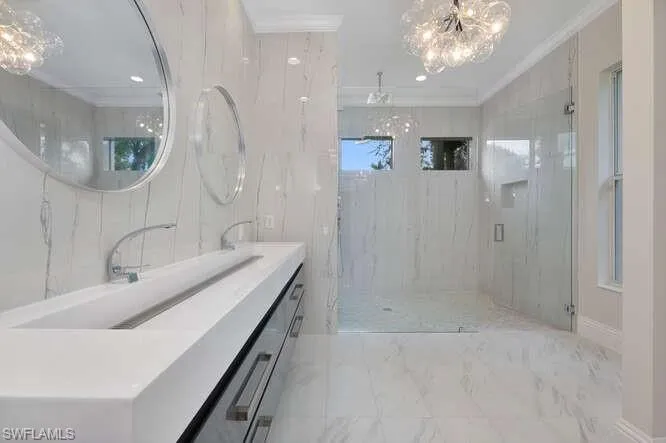 Full bathroom featuring crown molding, vanity, a chandelier, marble finish floor, and a marble finish shower