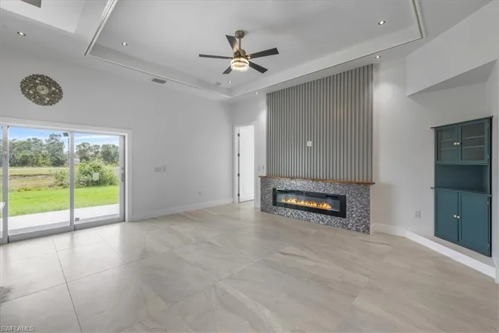 Unfurnished living room featuring ceiling fan, a tray ceiling, a tiled fireplace, a high ceiling, and baseboards