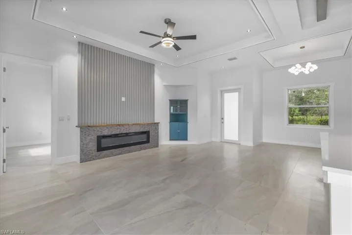 Unfurnished living room with a tray ceiling, ceiling fan, a glass covered fireplace, baseboards, and recessed lighting