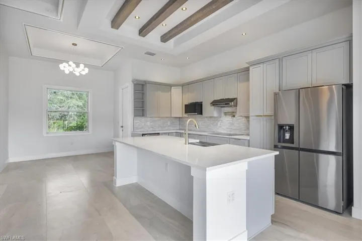 Kitchen featuring stainless steel refrigerator with ice dispenser, a sink, gray cabinetry, backsplash, and under cabinet range hood