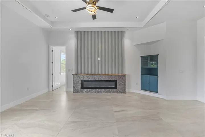 Unfurnished living room featuring a ceiling fan, a tray ceiling, a glass covered fireplace, recessed lighting, and baseboards