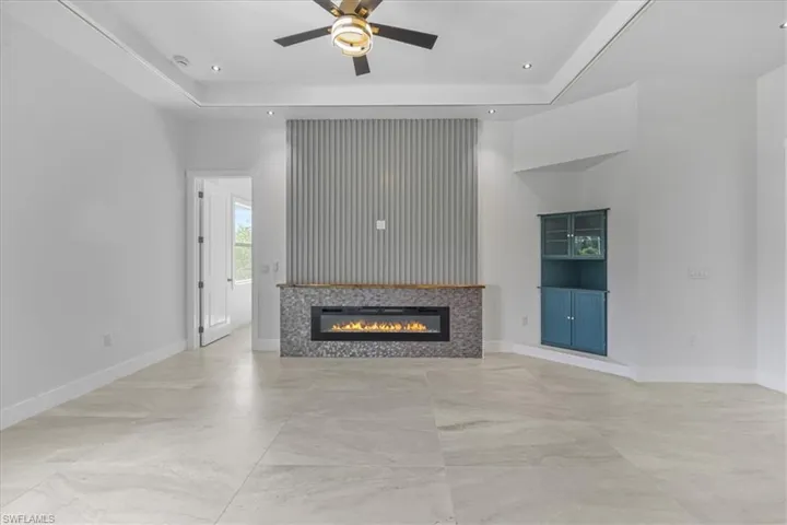 Unfurnished living room with a ceiling fan, a raised ceiling, a tiled fireplace, recessed lighting, and baseboards