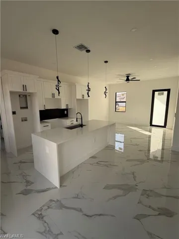 Modern kitchen featuring a waterfall island, white cabinetry, black backsplash, and black pendant lighting