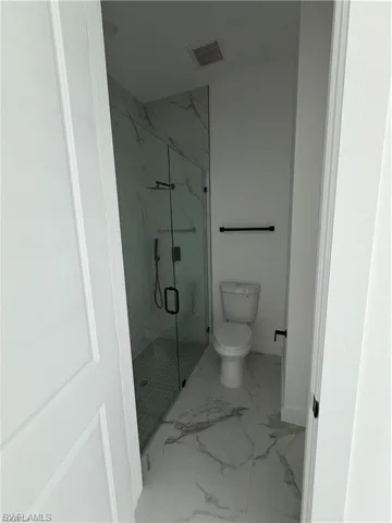 Bathroom featuring a glass-enclosed shower with contrasting floor tile, a wall-mounted towel bar, and a toilet
