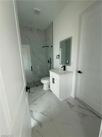 Contemporary bathroom featuring large format marble-look floor tile, a glass-enclosed shower with matching marble-look wall tile, a white vanity with integrated sink, and matte black fixtures
