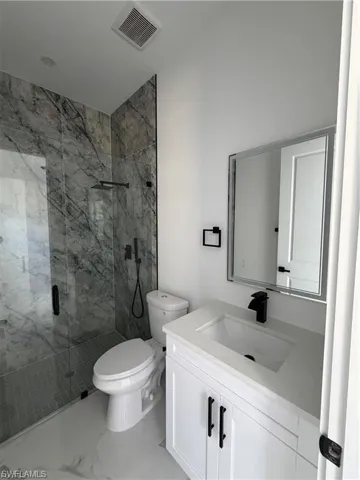 Modern bathroom featuring a walk-in shower with clear glass enclosure and gray marble-patterned tile, white vanity with integrated sink and matte black faucet, and white tile flooring