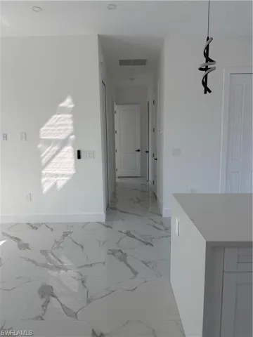 Spacious interior featuring modern tile flooring with a marble-effect pattern, white walls, recessed ceiling lighting, a contemporary pendant light fixture, and an integrated kitchen island with a light-colored countertop