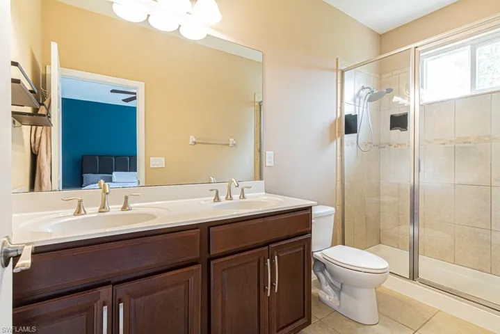 Bathroom with double sink vanity, a shower with shower door, tile patterned floors, and toilet