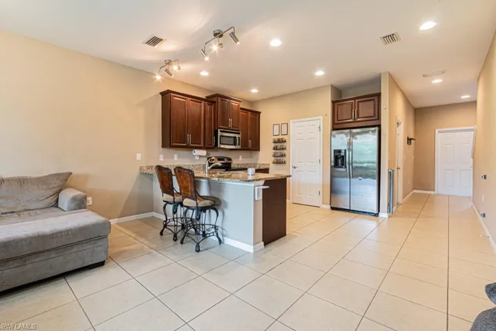 Kitchen featuring a kitchen breakfast bar, light tile patterned flooring, appliances with stainless steel finishes, light stone counters, and kitchen peninsula