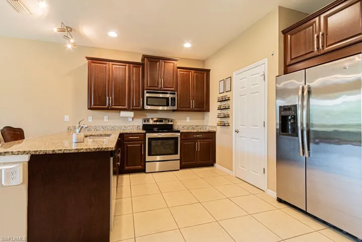 Kitchen with appliances with stainless steel finishes, light stone countertops, light tile patterned floors, sink, and kitchen peninsula