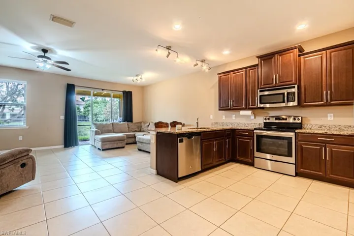 Kitchen featuring light stone counters, ceiling fan, appliances with stainless steel finishes, rail lighting, and sink