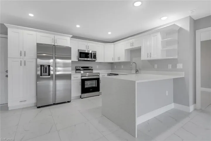 Kitchen featuring appliances with stainless steel finishes, kitchen peninsula, sink, and white cabinets