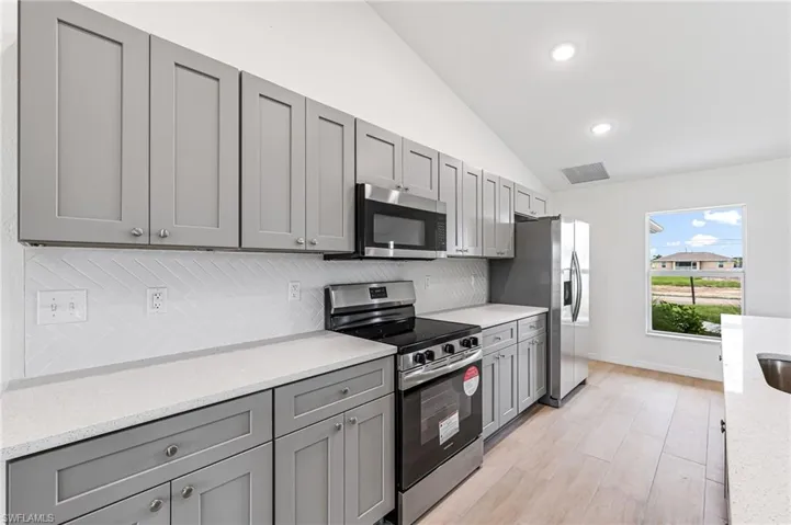 Kitchen featuring appliances with stainless steel finishes, vaulted ceiling, decorative backsplash, and gray cabinetry