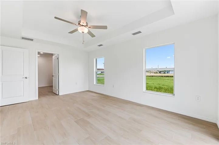 Spare room with light wood-style floors, a tray ceiling, visible vents, and baseboards